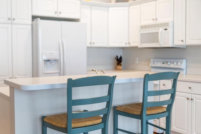 kitchen featuring white appliances, white cabinets, a breakfast bar area, and light countertops