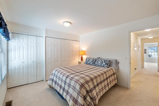 bedroom featuring two closets, light carpet, baseboards, and visible vents