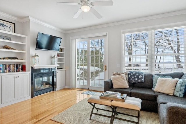 living room with light wood-type flooring, ornamental molding, ceiling fan, and a tile fireplace