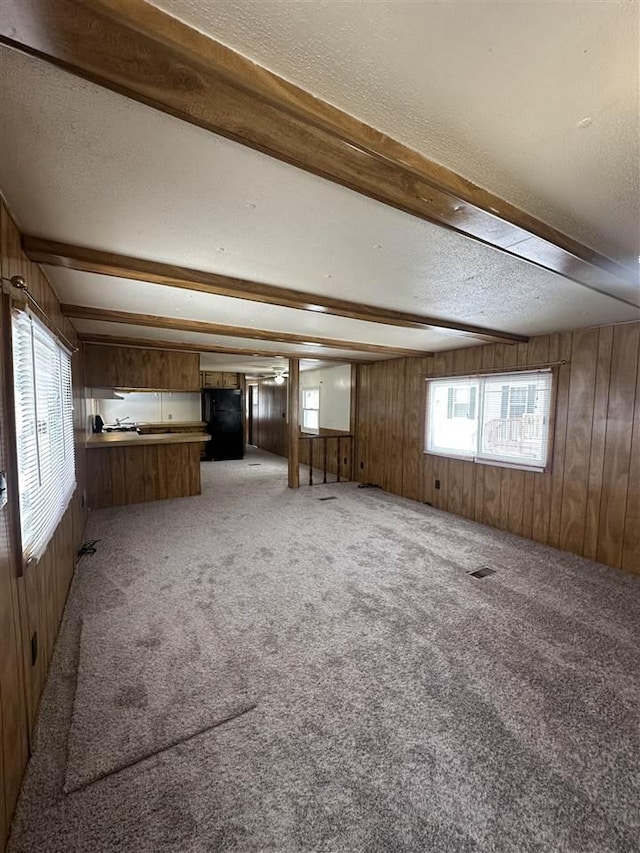 unfurnished room featuring beamed ceiling, light colored carpet, a textured ceiling, and wooden walls