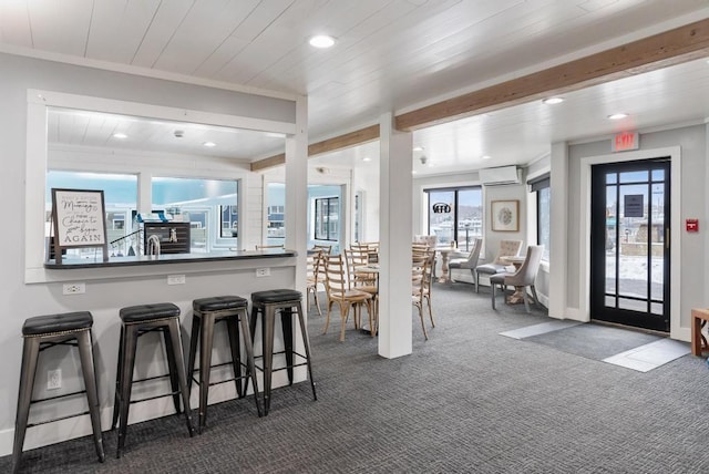 kitchen with an AC wall unit, a kitchen breakfast bar, ornamental molding, dark carpet, and beam ceiling