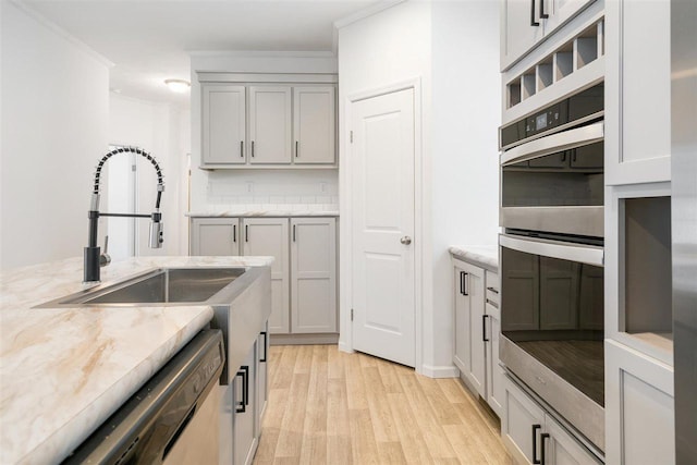 kitchen featuring gray cabinetry, light stone countertops, stainless steel appliances, and light wood-type flooring