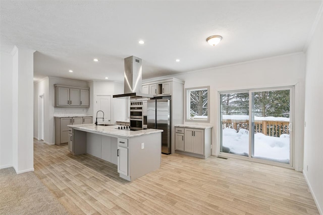 kitchen with appliances with stainless steel finishes, a kitchen island with sink, island range hood, and gray cabinetry