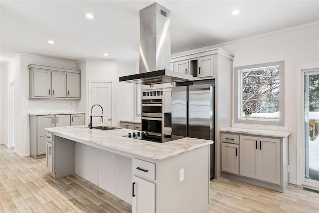 kitchen with sink, gray cabinetry, island range hood, appliances with stainless steel finishes, and a kitchen island with sink