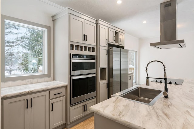 kitchen with appliances with stainless steel finishes, sink, gray cabinetry, island exhaust hood, and light stone counters