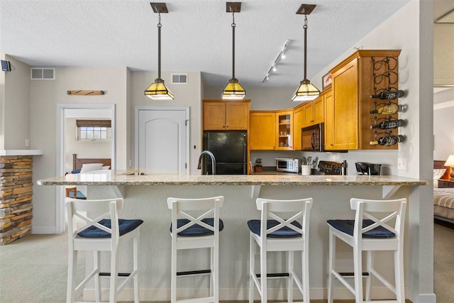 kitchen featuring light stone countertops, decorative light fixtures, black appliances, and kitchen peninsula