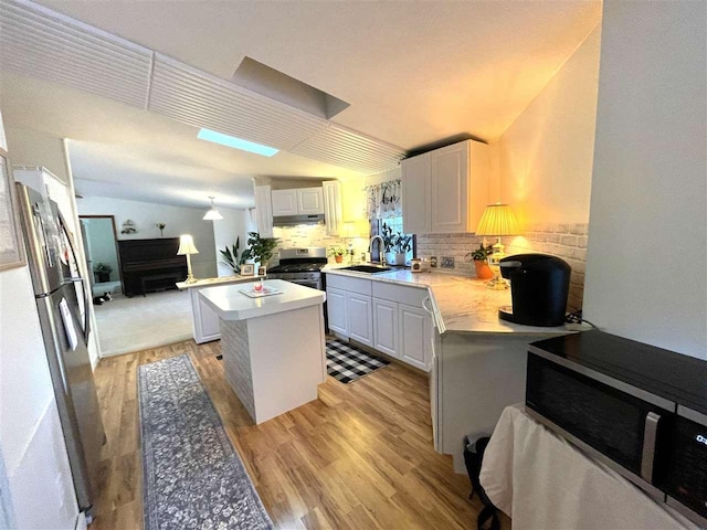 kitchen featuring appliances with stainless steel finishes, white cabinets, vaulted ceiling, and a center island