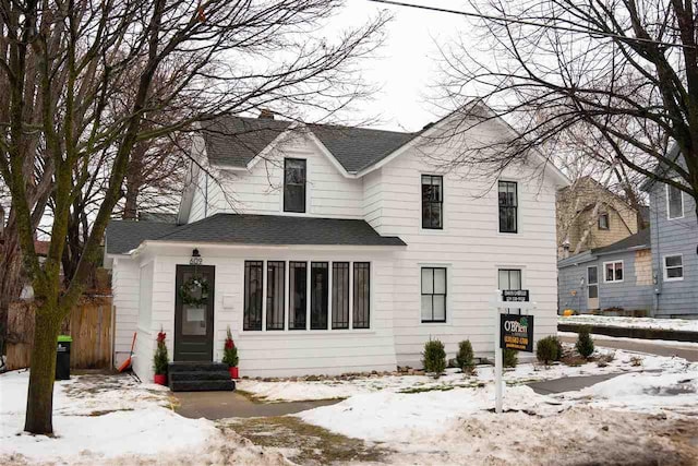 snow covered rear of property featuring a shingled roof