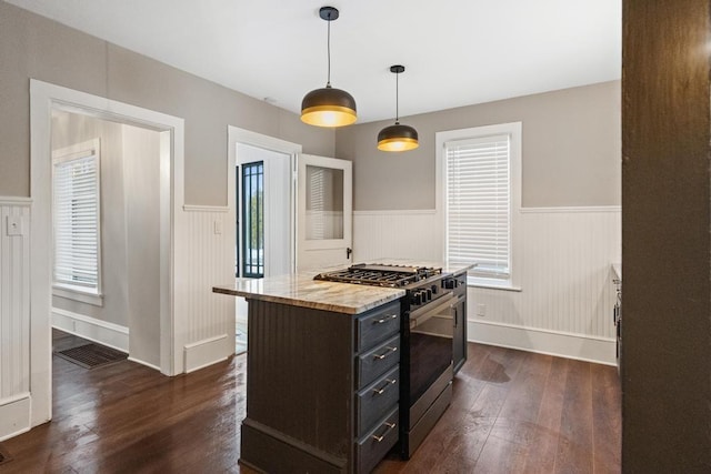 kitchen with stainless steel gas stove, wainscoting, dark wood finished floors, and decorative light fixtures