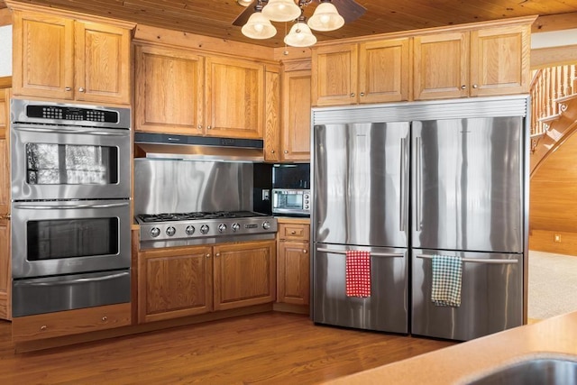 kitchen featuring built in appliances, light countertops, light wood-type flooring, under cabinet range hood, and a warming drawer