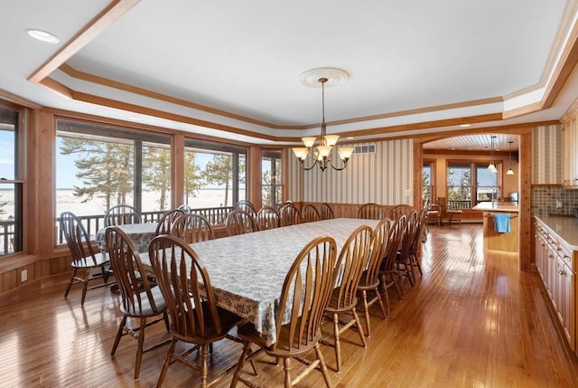 dining space featuring crown molding, a raised ceiling, light wood-style flooring, and a notable chandelier