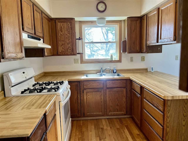 kitchen with brown cabinets, gas range gas stove, light countertops, a sink, and under cabinet range hood