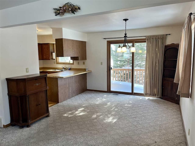 kitchen with light colored carpet, a peninsula, light countertops, pendant lighting, and a sink