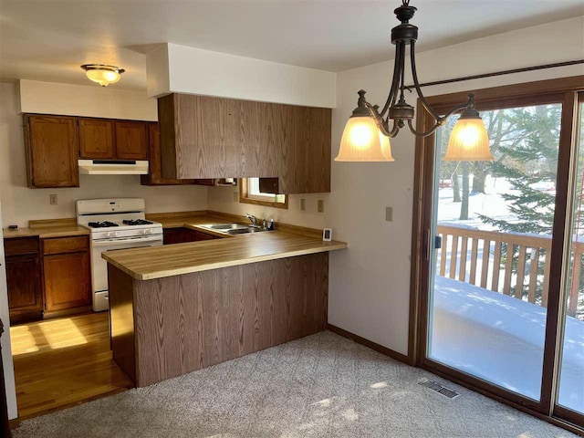 kitchen with under cabinet range hood, a peninsula, hanging light fixtures, light countertops, and white gas range