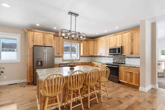 kitchen with stainless steel appliances, a center island, decorative light fixtures, and light stone countertops