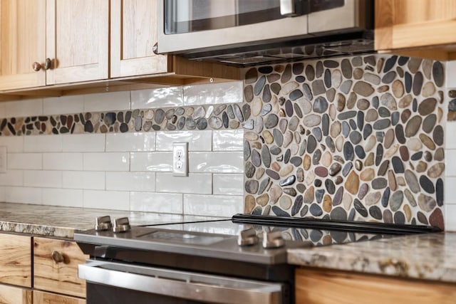 kitchen featuring stone countertops, stainless steel microwave, backsplash, and light brown cabinetry