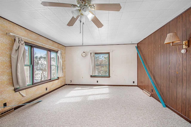 spare room featuring carpet, visible vents, a ceiling fan, wooden walls, and baseboards