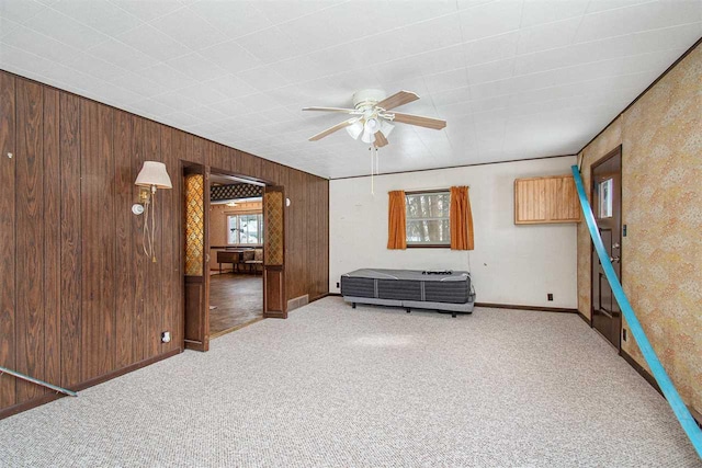 unfurnished living room featuring visible vents, carpet flooring, ceiling fan, wooden walls, and baseboards