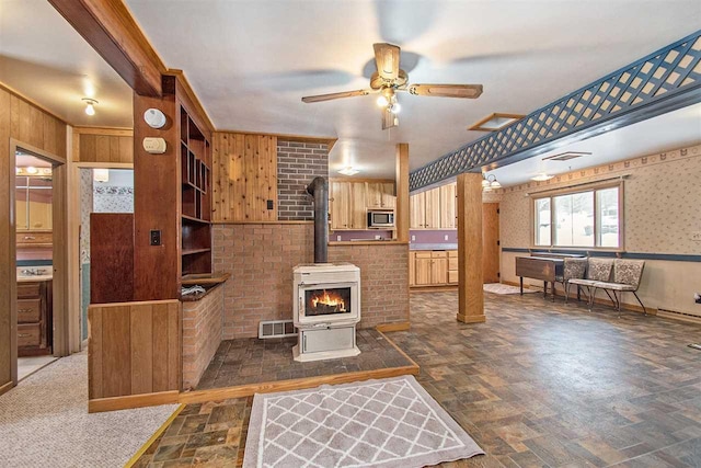 living room featuring visible vents, ceiling fan, wood walls, and a wood stove