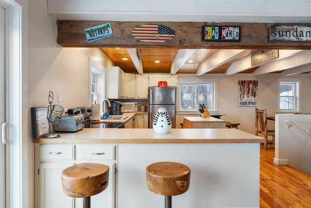 kitchen with freestanding refrigerator, light countertops, a peninsula, and a breakfast bar area