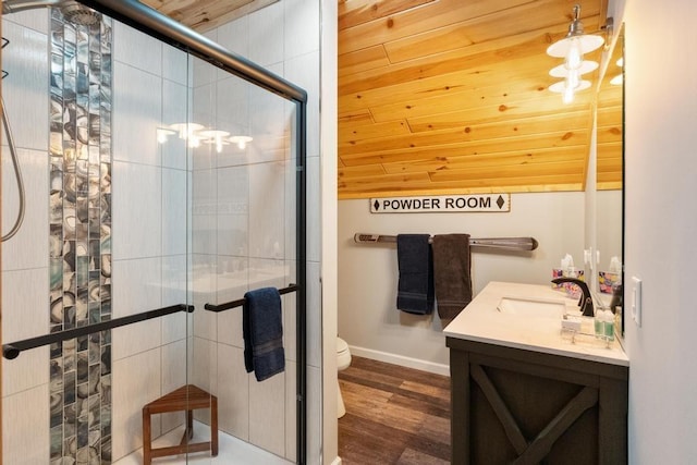 bathroom with toilet, a stall shower, vanity, wood finished floors, and baseboards