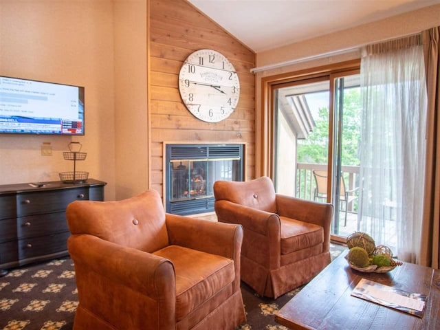 living room with vaulted ceiling, a glass covered fireplace, and wooden walls