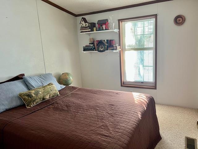 carpeted bedroom featuring ornamental molding, multiple windows, and visible vents