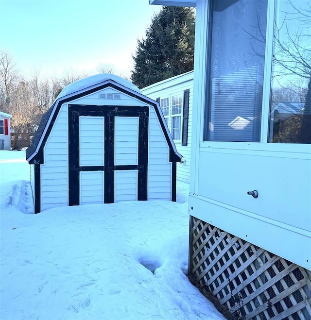 snow covered property featuring an outdoor structure, a gambrel roof, and a storage unit