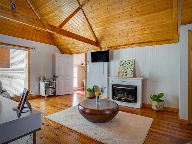 living room featuring lofted ceiling with beams, a glass covered fireplace, wood ceiling, baseboards, and hardwood / wood-style flooring