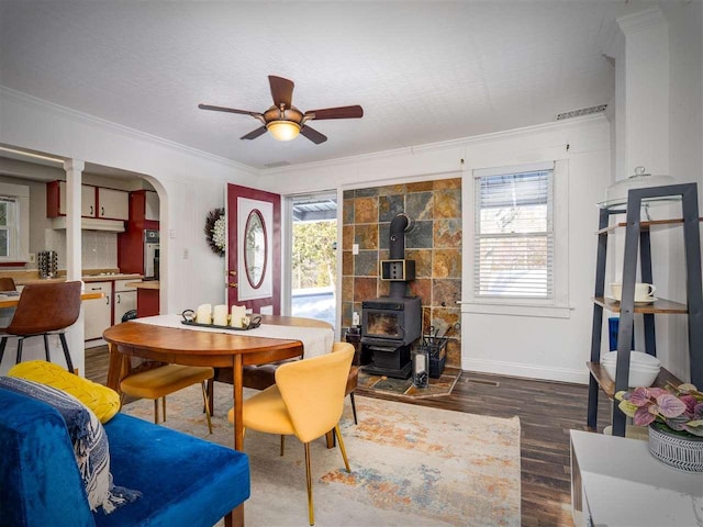 dining room with arched walkways, a wood stove, crown molding, and dark wood-style flooring