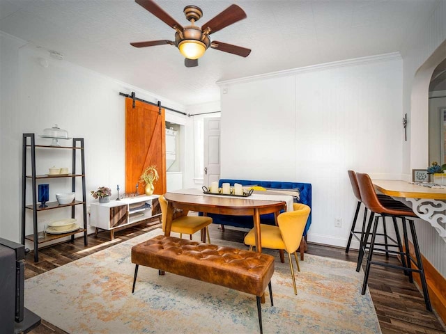 dining space with a barn door, arched walkways, a ceiling fan, ornamental molding, and wood finished floors