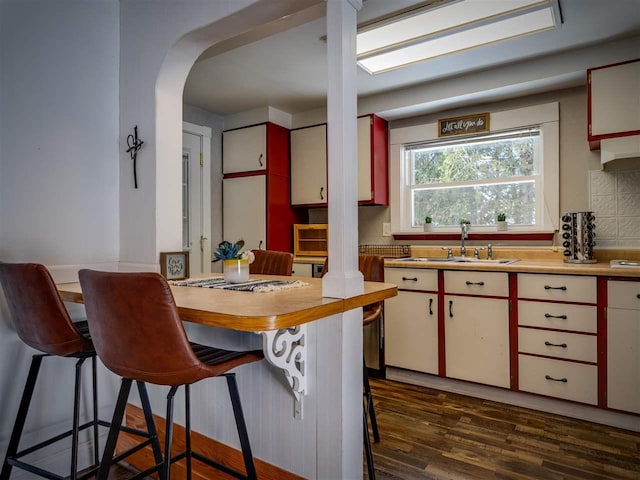 kitchen with a breakfast bar, arched walkways, dark wood-style flooring, light countertops, and a sink