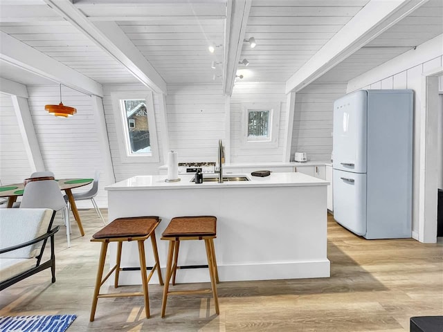 kitchen with a sink, light countertops, beam ceiling, freestanding refrigerator, and light wood finished floors