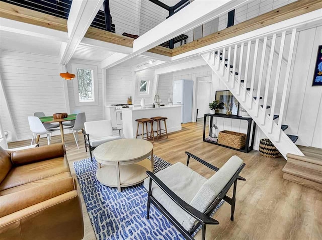 living area featuring stairway, wooden walls, light wood-type flooring, coffered ceiling, and beamed ceiling