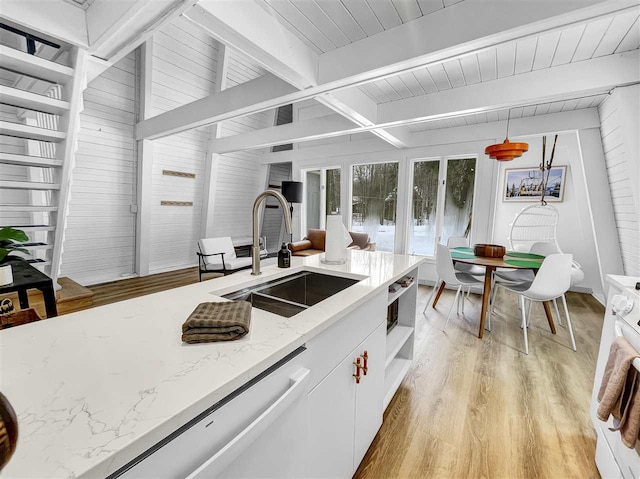 kitchen with light wood-type flooring, beam ceiling, white cabinets, and a sink