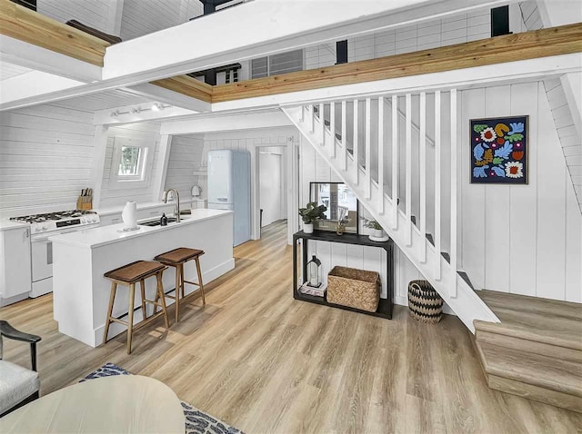 interior space featuring light wood-style floors, beam ceiling, wood walls, and stairway