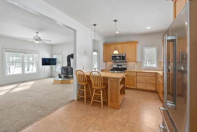 kitchen featuring light colored carpet, open floor plan, a peninsula, stainless steel appliances, and a kitchen bar