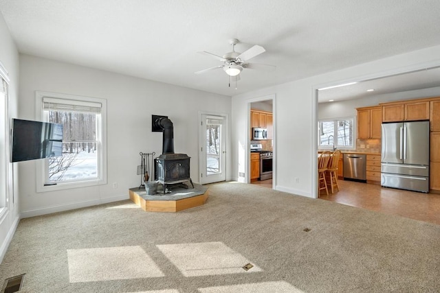 living area featuring recessed lighting, visible vents, a wood stove, light carpet, and baseboards