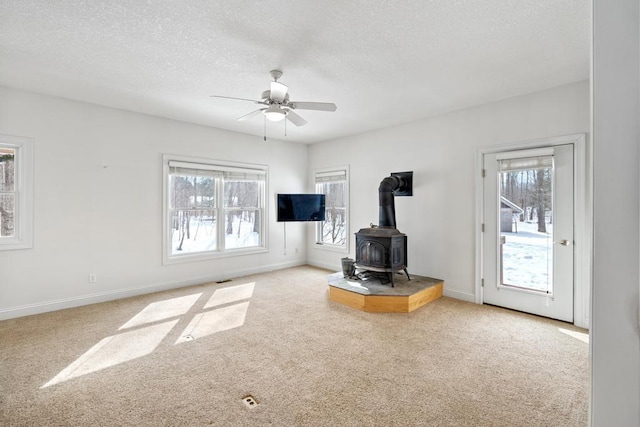 unfurnished living room featuring a textured ceiling, ceiling fan, carpet floors, baseboards, and a wood stove