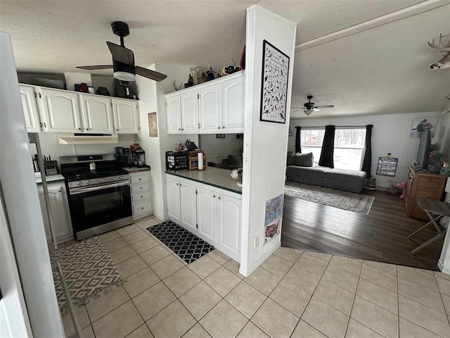 kitchen with stainless steel range with gas cooktop, white cabinets, under cabinet range hood, and light tile patterned floors