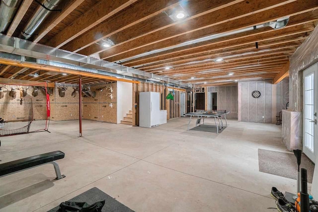 unfinished basement featuring stairway and freestanding refrigerator