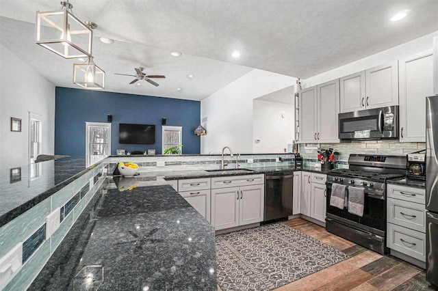 kitchen with wood finished floors, a sink, appliances with stainless steel finishes, decorative backsplash, and dark stone countertops