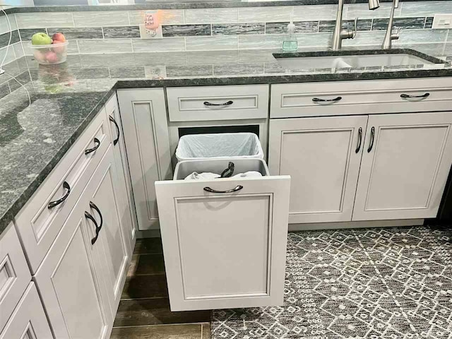 interior details with dark stone counters, white cabinetry, a sink, and decorative backsplash