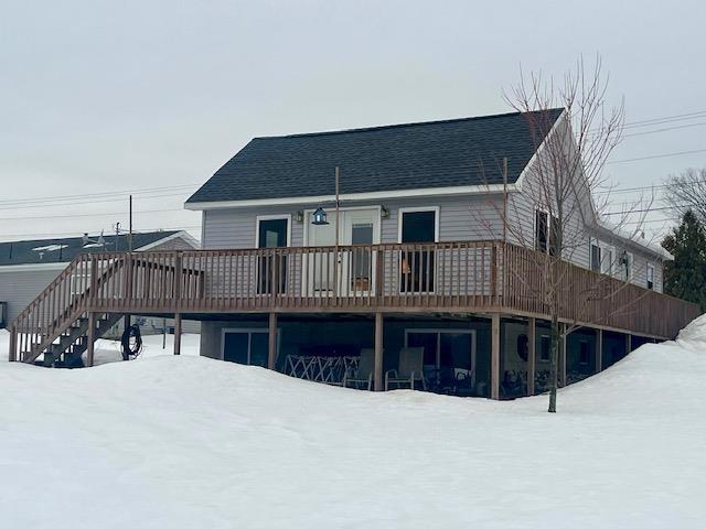 snow covered property with roof with shingles, a wooden deck, and stairs