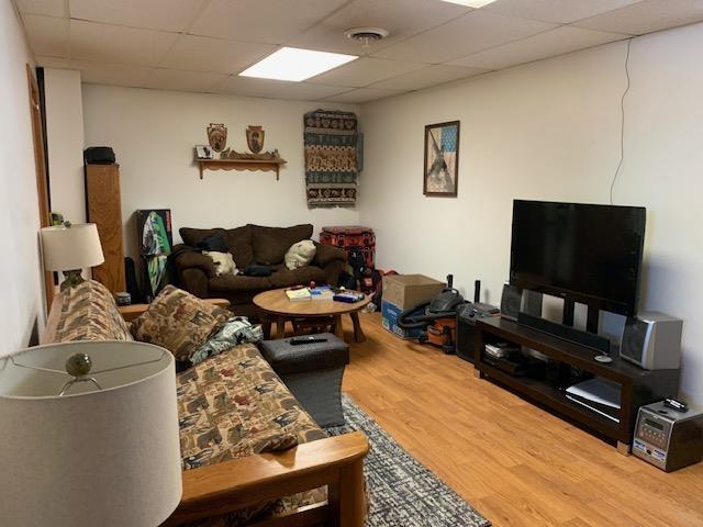 living area with a paneled ceiling, visible vents, and wood finished floors