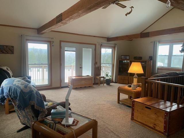 carpeted living room featuring a wealth of natural light, french doors, vaulted ceiling with beams, and ceiling fan