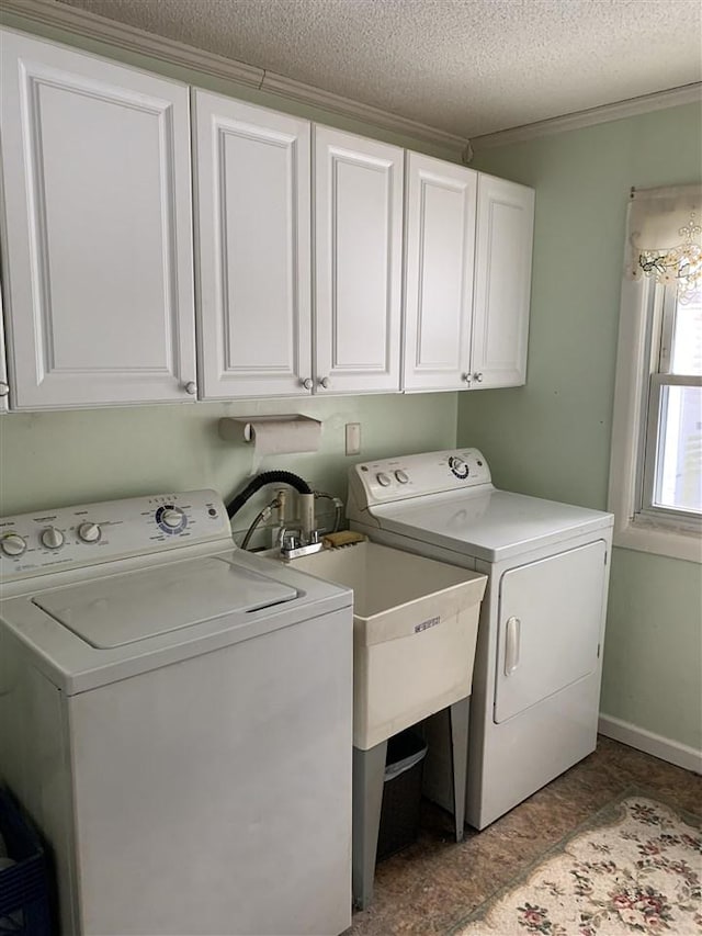 laundry room featuring a textured ceiling, baseboards, ornamental molding, cabinet space, and washer and clothes dryer