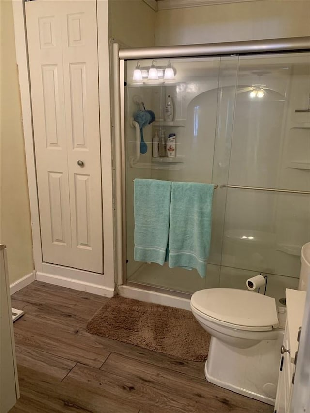 bathroom with baseboards, wood finished floors, toilet, and a shower stall