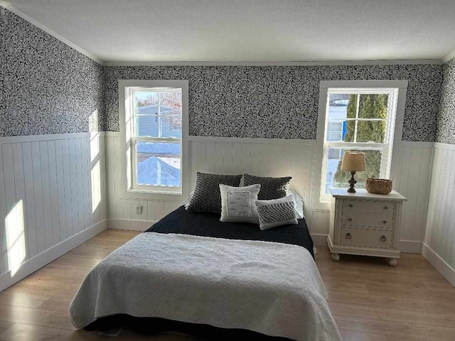 bedroom with a wainscoted wall, light wood finished floors, and wallpapered walls