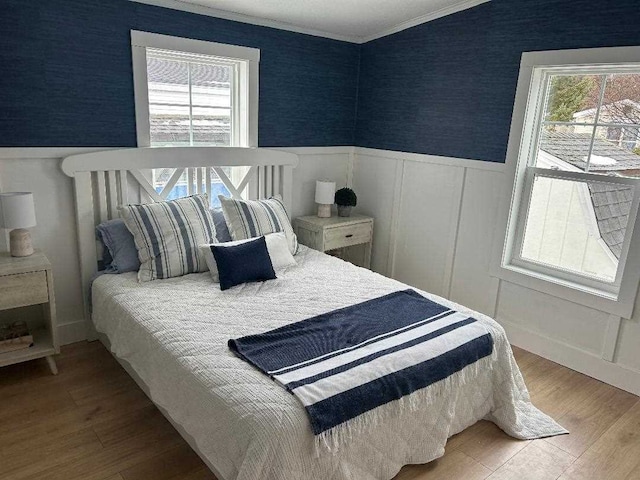 bedroom featuring a wainscoted wall, crown molding, multiple windows, and wood finished floors